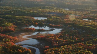 AX149_156 - 5.5K aerial stock footage flying high over a pond and colorful forest in autumn, Belfast, Maine, sunset