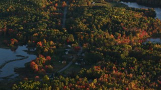AX149_159 - 5.5K aerial stock footage flying by pond and homes among colorful forest in autumn, Belfast, Maine, sunset