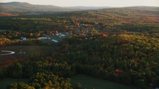 AX149_174 - 5.5K aerial stock footage approaching small rural town, colorful trees in autumn, Searsmont, Maine, sunset