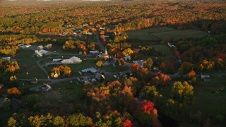 AX149_177E - 5.5K aerial stock footage orbiting small rural town near colorful forest, autumn, Searsmont, Maine, sunset