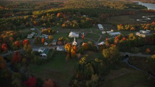 AX149_179E - 5.5K aerial stock footage orbiting a small rural town, colorful trees in autumn, Searsmont, Maine, sunset