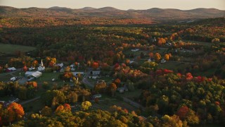 AX149_183 - 5.5K stock footage aerial video orbiting church, small rural town, colorful trees in autumn, Searsmont, Maine, sunset