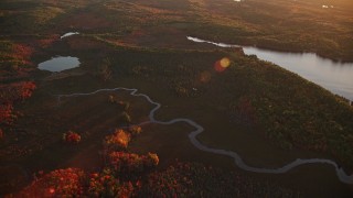 AX149_197E - 5.5K aerial stock footage flying by rivers near pond, colorful forest in autumn, Palermo, Maine, sunset