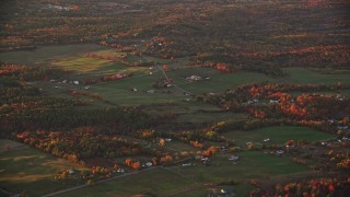 AX149_204E - 5.5K aerial stock footage flying by small farms, colorful trees in autumn, Windsor, Maine, sunset