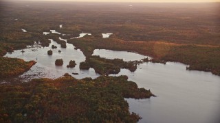 AX149_209E - 5.5K aerial stock footage flying by Togus Pond, dense colorful forest, autumn, Augusta, Maine, sunset