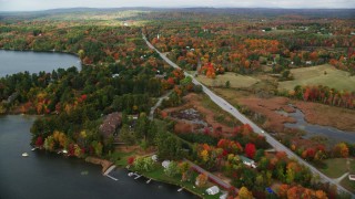 AX150_007 - 5.5K aerial stock footage flying by colorful foliage, waterfront homes, Western Avenue, autumn, Winthrop, Maine