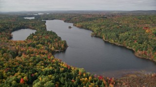 AX150_010E - 5.5K aerial stock footage flying over colorful forest, approach Upper Narrows Pond, autumn, Winthrop, Maine