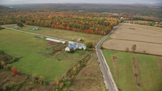 AX150_034E - 5.5K aerial stock footage flying over colorful trees, approaching a farm, autumn, Leeds, Maine
