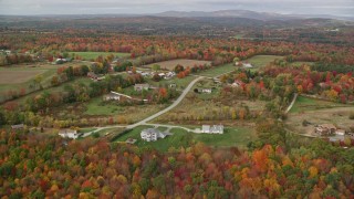AX150_039 - 5.5K aerial stock footage flying over colorful trees, approaching farm, rural homes, autumn,Turner, Maine