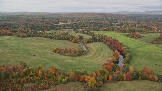 AX150_041 - 5.5K aerial stock footage flying by Nezinscot River, colorful trees, green fields, autumn, Turner, Maine