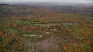 AX150_073E - 5.5K aerial stock footage flying over colorful forest, tilt up, reveal rural residential area, autumn, Paris, Maine