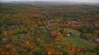 AX150_075E - 5.5K aerial stock footage flying over colorful forest, rural homes, Buckfield Road, autumn, Paris, Maine