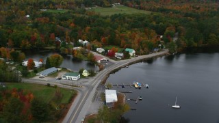 AX150_101 - 5.5K stock footage aerial video tilting down on waterfront rural homes, store in autumn, Lake Pennesseewassee, Norway, Maine