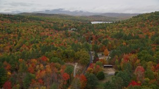 AX150_129E - 5.5K aerial stock footage flying over brightly colored forest, rural homes, Maine Street, Keewaydin Lake, autumn, Stoneham, Maine