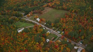 AX150_137E - 5.5K aerial stock footage flying over forest, approach Cezar Lake, tilt down on rural homes, autumn, overcast, Lovell, Maine