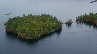 AX150_139 - 5.5K stock footage aerial video flying by Sheep Island waterfront home, colorful trees, Kezar Lake, autumn, Lovell, Maine
