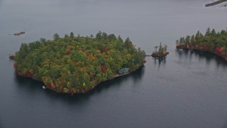 AX150_139E - 5.5K aerial stock footage flying by Sheep Island waterfront home, colorful trees, Kezar Lake, autumn, Lovell, Maine