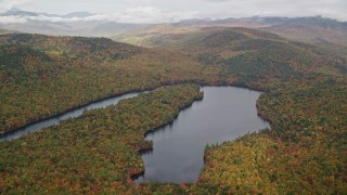 AX150_143E - 5.5K aerial stock footage flying by Horseshoe Pond, dense forest, hills, autumn, overcast, Lovell, Maine
