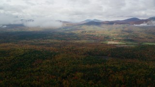 AX150_145 - 5.5K aerial stock footage flying over colorful forest, approach White Mountains, cloudy, autumn, Stow, Maine