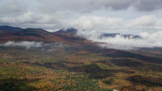 AX150_149 - 5.5K aerial stock footage flying over colorful forest, autumn, by clouds, White Mountains, New Hampshire