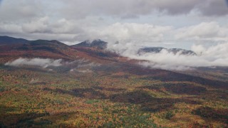 AX150_149E - 5.5K aerial stock footage flying over colorful forest, autumn, by clouds, White Mountains, New Hampshire