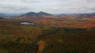 AX150_152 - 5.5K aerial stock footage flying over forest, cloudy, autumn, approach Mountain Pond, White Mountains, New Hampshire