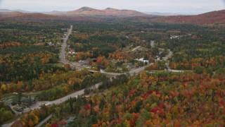 AX150_217E - 5.5K aerial stock footage flying over Highway 302, forest, approach small town, autumn, Carroll, New Hampshire