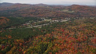AX150_238E - 5.5K aerial stock footage flying over colorful forest, approach small rural town, autumn, Franconia, New Hampshire