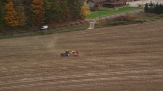 AX150_291 - 5.5K aerial stock footage tracking a tractor on farmland, colorful trees in autumn, Woodsville, New Hampshire
