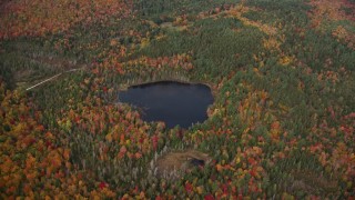AX150_318E - 5.5K aerial stock footage approaching pond, colorful forest and tilt down, autumn, Topsham, Vermont
