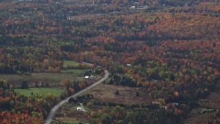 AX150_324 - 5.5K aerial stock footage flying by rural homes, Highway 302 through forest, autumn, overcast, Topsham, Vermont