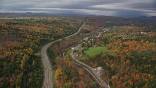 AX150_346E - 5.5K aerial stock footage flying over Route 62,  Main Street near rural homes, colorful forest in autumn, Barre, Vermont