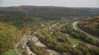 AX150_425E - 5.5K aerial stock footage flying over colorful forest, hills, approach small farms and river, autumn, South Royalton, Vermont