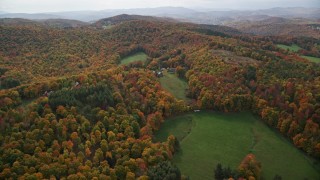AX150_460 - 5.5K aerial stock footage flying over colorful forest, hills, approach rural home, tilt down, autumn, North Pomfret, Vermont