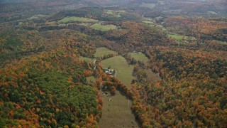AX150_464E - 5.5K aerial stock footage flying over brightly colored forest, approaching a farm, autumn, Quechee, Vermont