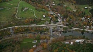 AX151_008E - 5.5K aerial stock footage approaching small rural town, tilt down over bridge spanning Ottauquechee River, autumn, Taftsville, Vermont