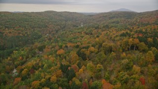 AX151_037E - 5.5K aerial stock footage flying over brightly colored forested hills, approach rural homes, autumn, Taftsville, Vermont