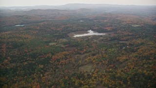 AX151_071E - 5.5K aerial stock footage flying over forested hills, approaching pond, overcast, autumn, Croydon, New Hampshire