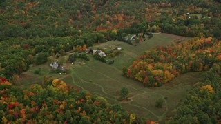 AX151_140 - 5.5K aerial stock footage approaching rural homes, grassy clearing, tilt down, autumn, Penacook, New Hampshire