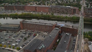 AX152_100E - 5.5K aerial stock footage flying by factory near bridge spanning river, autumn, Lawrence, Massachusetts