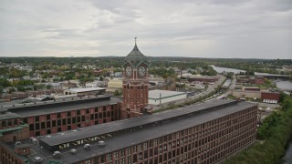 AX152_102E - 5.5K aerial stock footage of a factory and clock tower by the water, overcast, Lawrence, Massachusetts