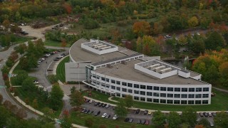 AX152_118E - 5.5K aerial stock footage passing by an office building among fall foliage, autumn, Andover, Massachusetts