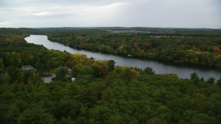AX152_121 - 5.5K aerial stock footage flying over trees with fall colors toward a river with kayakers, autumn, Andover, Massachusetts