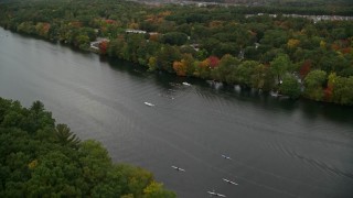 AX152_121E - 5.5K aerial stock footage flying over trees with fall colors toward a river with kayakers, autumn, Andover, Massachusetts