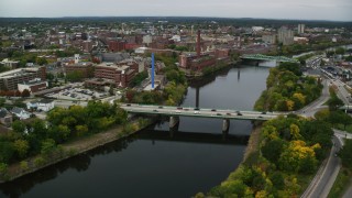 AX152_128 - 5.5K aerial stock footage flying over bridge on a river toward abandoned factory, autumn, Lowell, Massachusetts