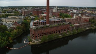 AX152_129 - 5.5K aerial stock footage flying by riverside abandoned factory and smoke stack, autumn, Lowell, Massachusetts