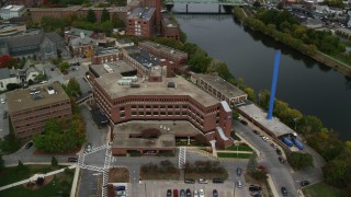 AX152_133 - 5.5K aerial stock footage flying by Saints Medical Center near the river, blue smoke stack, autumn, Lowell, Massachusetts