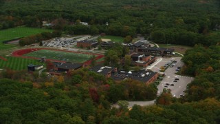 AX152_205 - 5.5K aerial stock footage flying away from high school and football field among fall foliage, Dover, Massachusetts