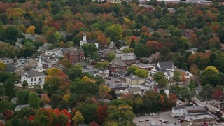 AX152_206E - 5.5K aerial stock footage flying over fall foliage toward churches in a town, Medfield, Massachusetts