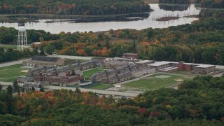 AX152_210E - 5.5K aerial stock footage of a slow approach over fall foliage toward Massachusetts Correctional Institution at Norfolk, Massachusetts